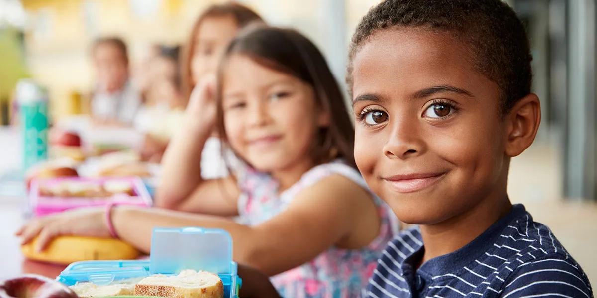 A little boy eats lunch sitting with his friends