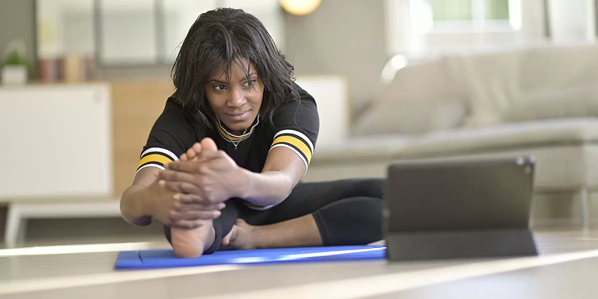 An African American woman, presumably in a Steelers jersey, stretches while watching Virtual Y