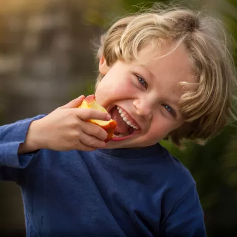 Pre-K aged, blonde-haired kid eats an apple while smiling