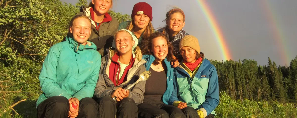 Seven teens sitting under a double rainbow