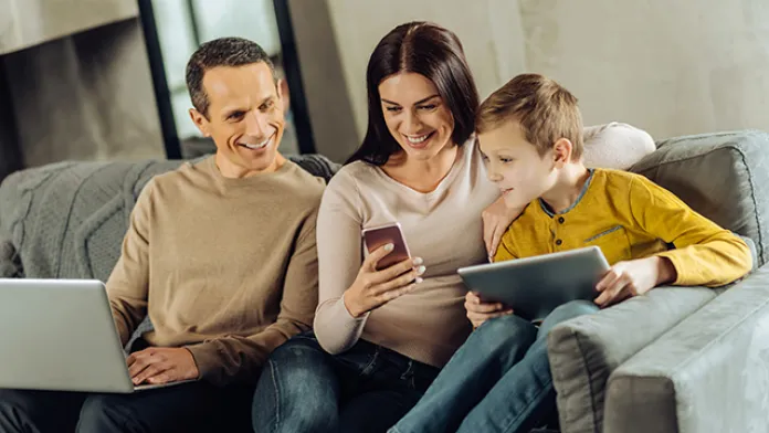 Family using the YMCA360 app on multiple devices, including tablet, smartphone, and laptop.